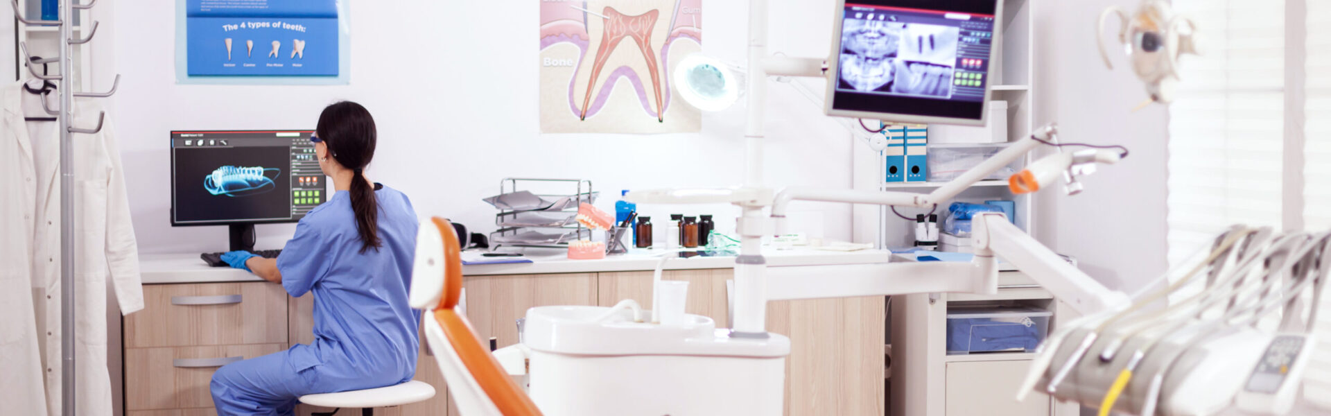 Stomatology office with modern equipment and nurse wearing blue uniform working on computer.